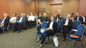 The Polish audience pays rapt attention to the scientific argument presented by the Spanish, Polish, and American speakers